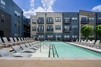 A swimming pool surrounded by lounge chairs in front of apartment buildings.